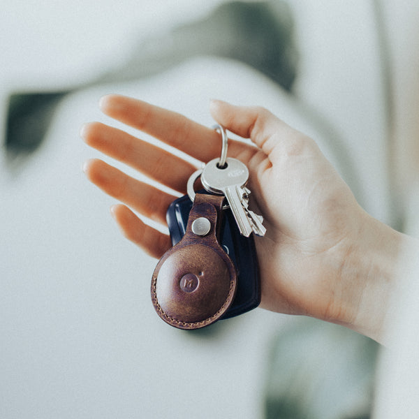 Hand holding a set of keys with a leather air tag keychain