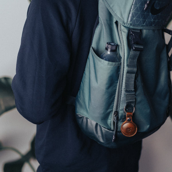 Man carrying a backpack with a leather air tag holder chained on it