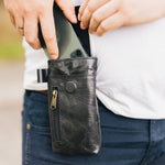 man placing a mobile phone in a black leather phone holster clipped on his waist