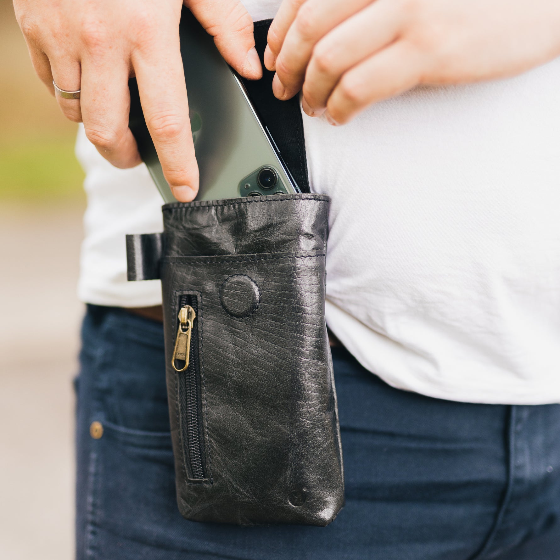 man placing a mobile phone in a black leather phone holster clipped on his waist