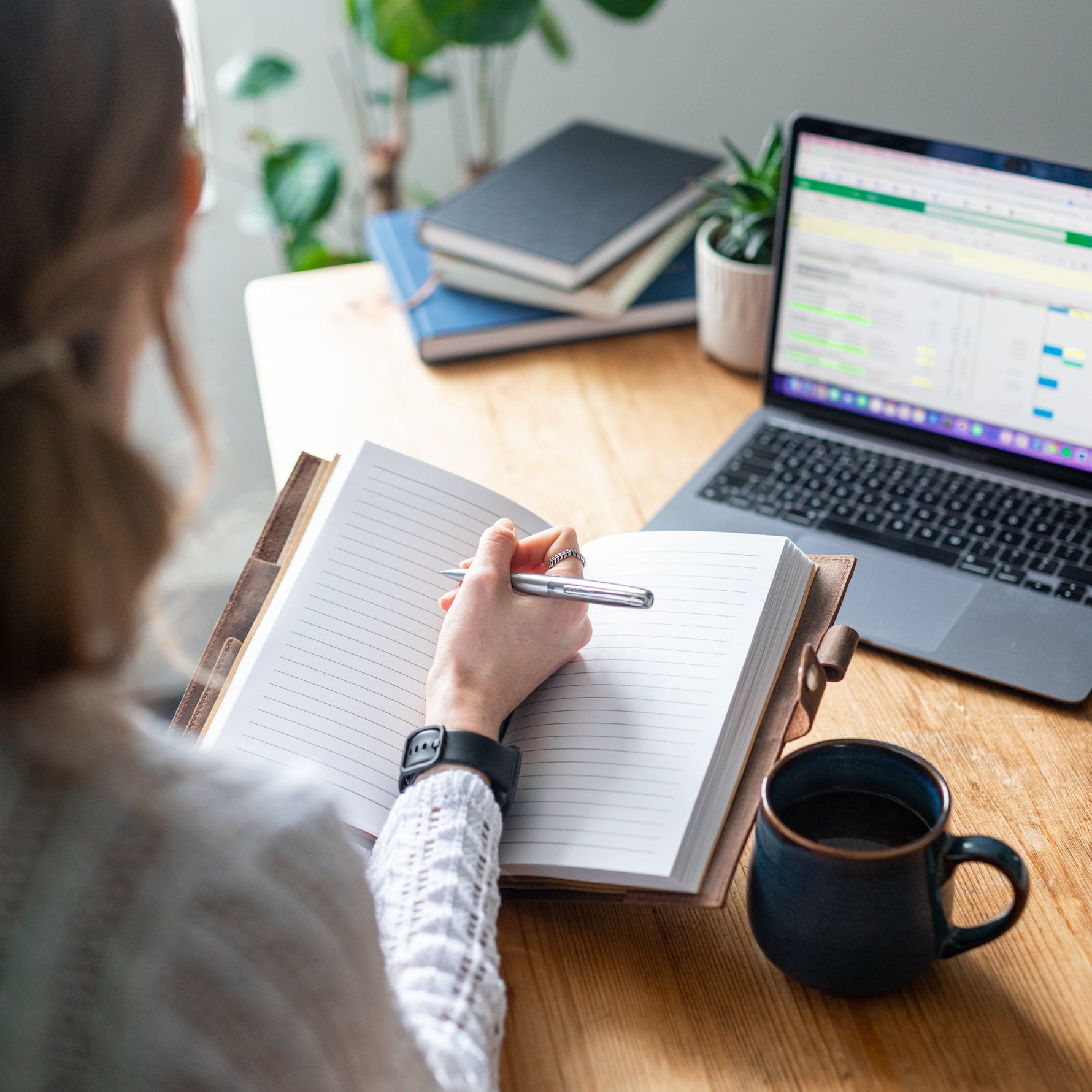 Woman holding a pen over a lined leather journal on an office desk