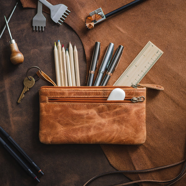 Light brown leather pencil case filled with pens, pencils and with a key attached