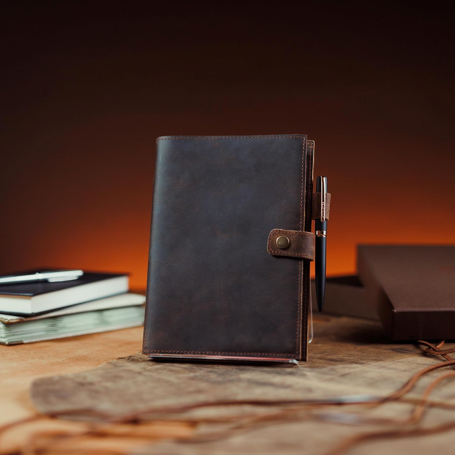 Brown leather notebook with pen holder on a wooden surface with a warm-toned background