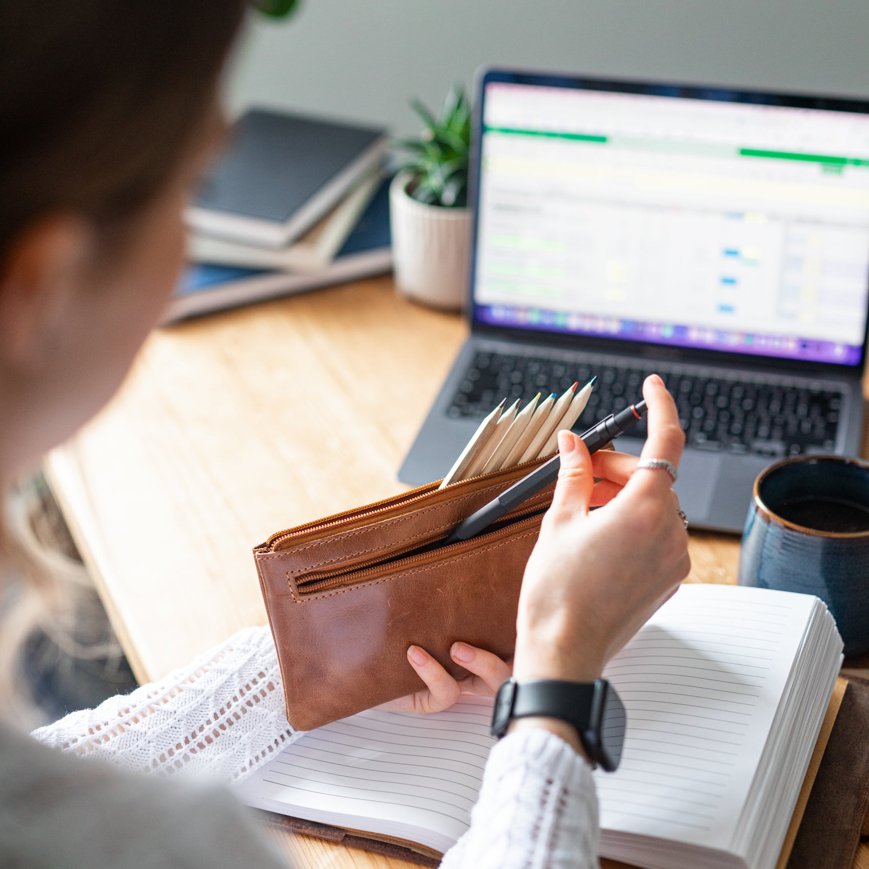 Woman placing a pen in light brown leather pencil case